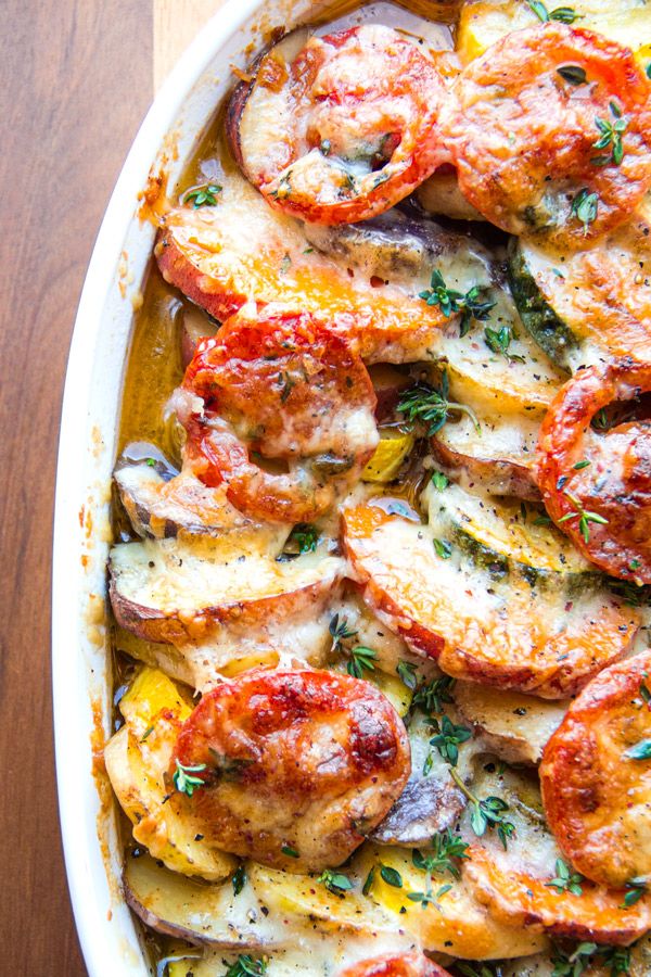 a casserole dish with chicken, tomatoes and mushrooms in it on a wooden table