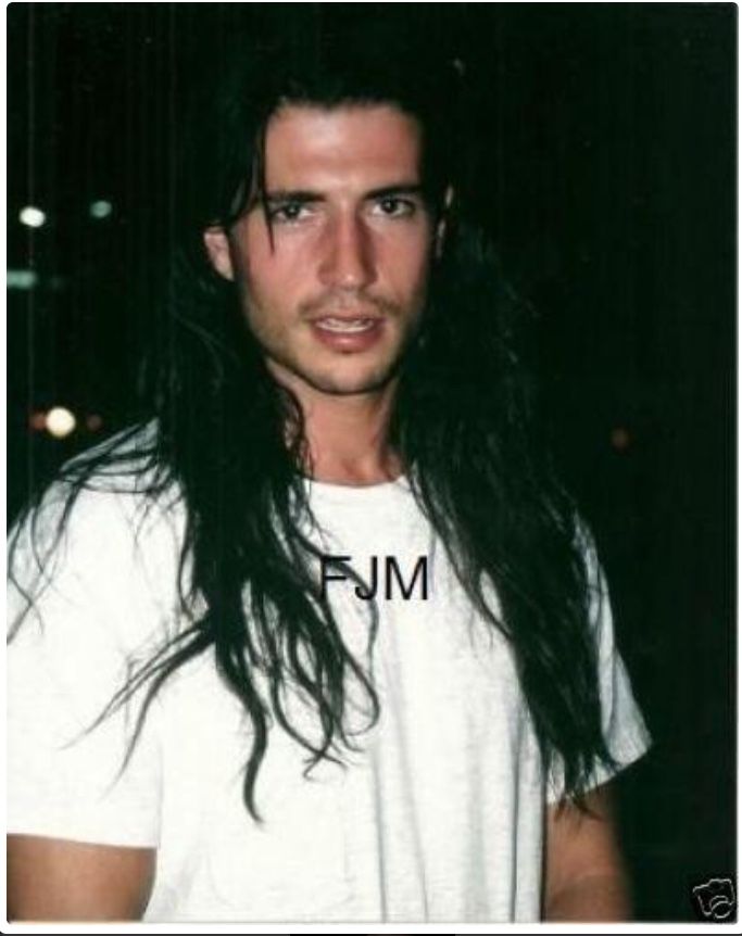 a man with long black hair wearing a white shirt