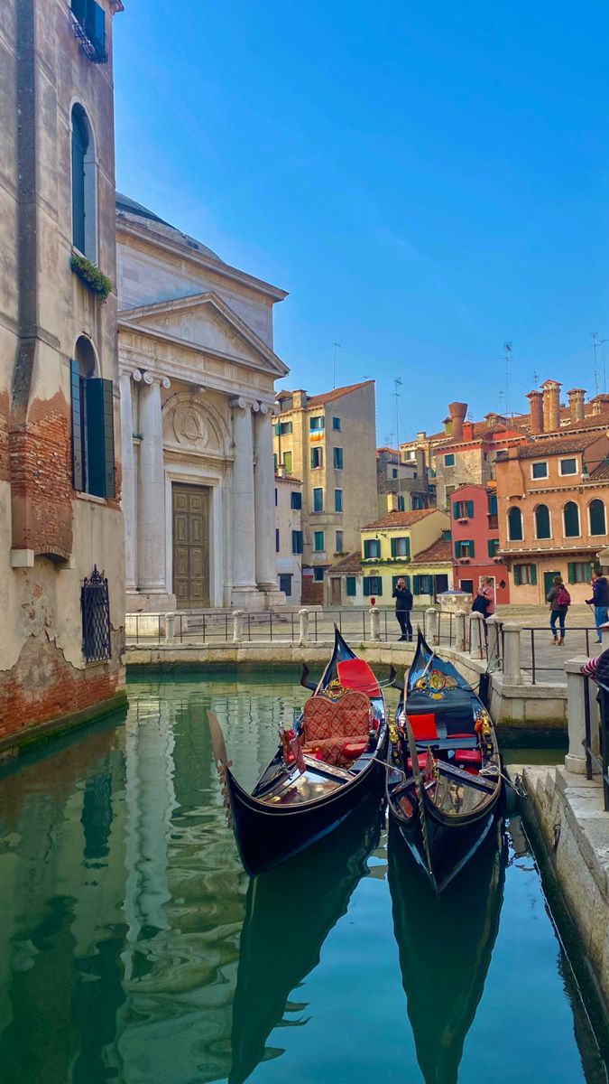 two gondolas are tied to the side of a canal with buildings in the background