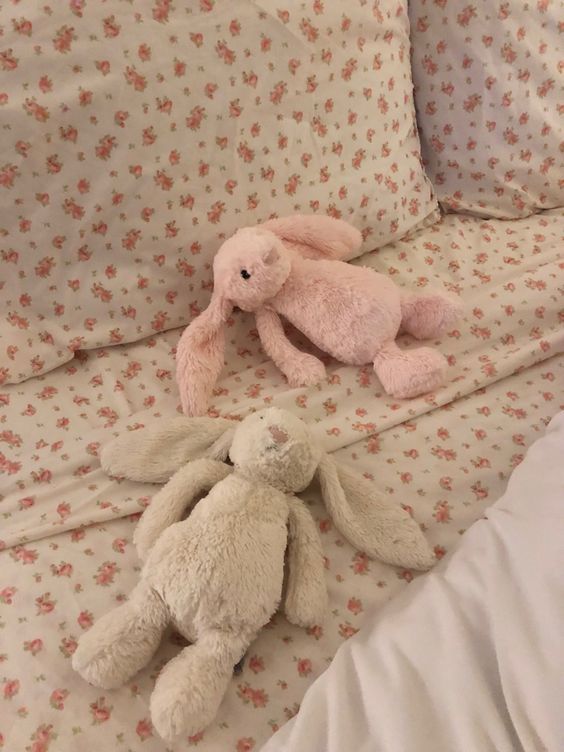 two stuffed animals laying on top of a bed next to pillows and sheets with pink flowers