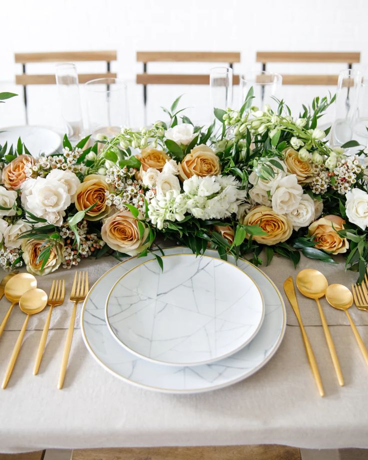 the table is set with gold and white plates, silverware, and floral centerpieces