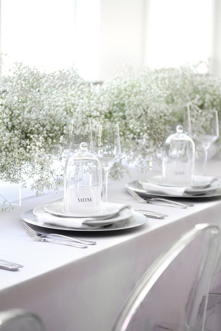 the table is set with silverware and baby's breath flowers in glass vases