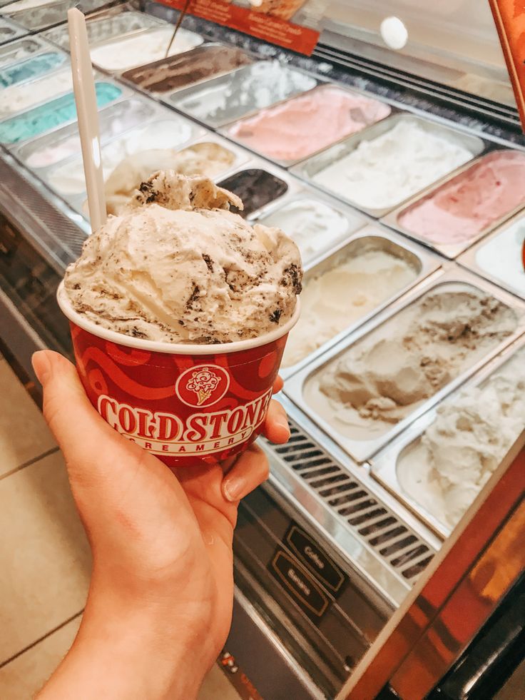 a person holding up an ice cream sundae in front of a store display case