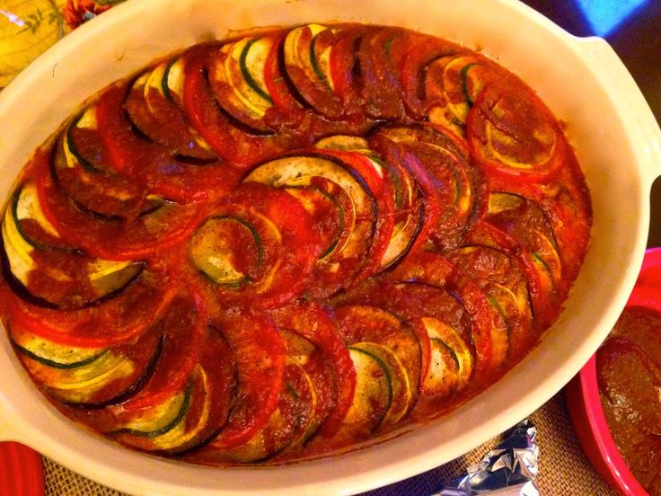 a casserole dish with red sauce and sliced vegetables