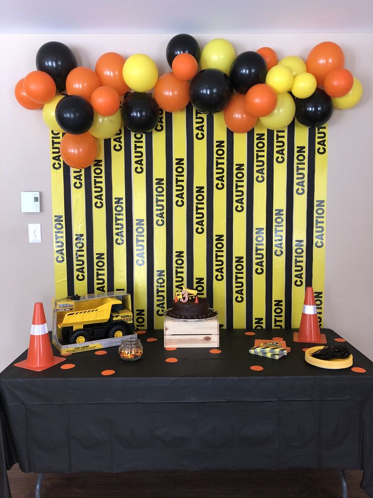 a table topped with black and orange balloons next to a yellow sign that reads construction zone