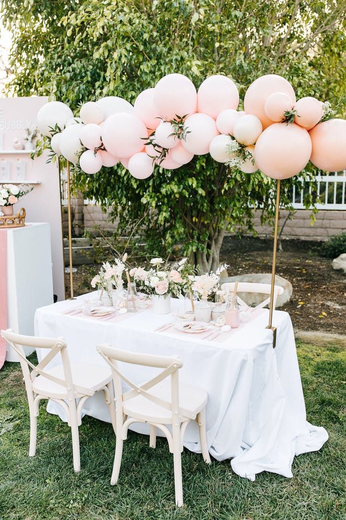 a table set up for a party with pink balloons and white linens on it