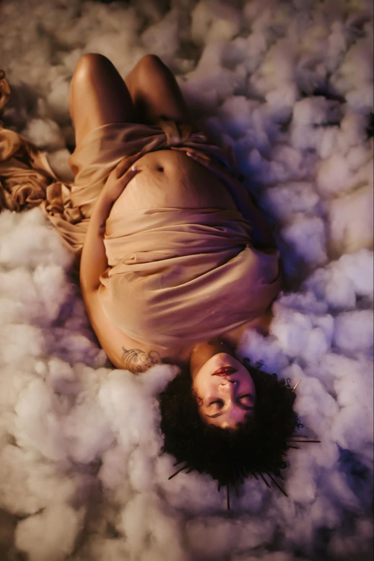 a woman laying on the ground surrounded by clouds of cotton flecked around her