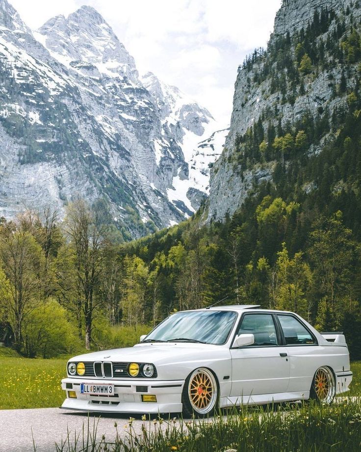 a white car parked on the side of a road in front of some snow covered mountains