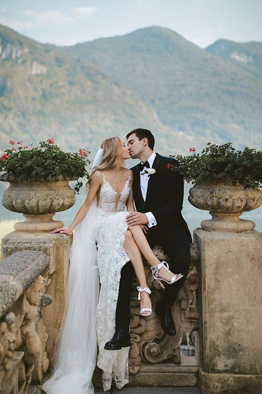 a bride and groom are sitting on a stone wall with flowers in the vases