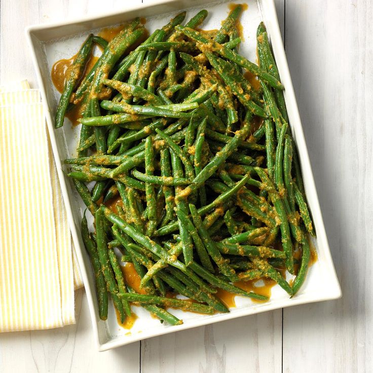 green beans with mustard sauce in a white square dish on a wooden table next to a napkin