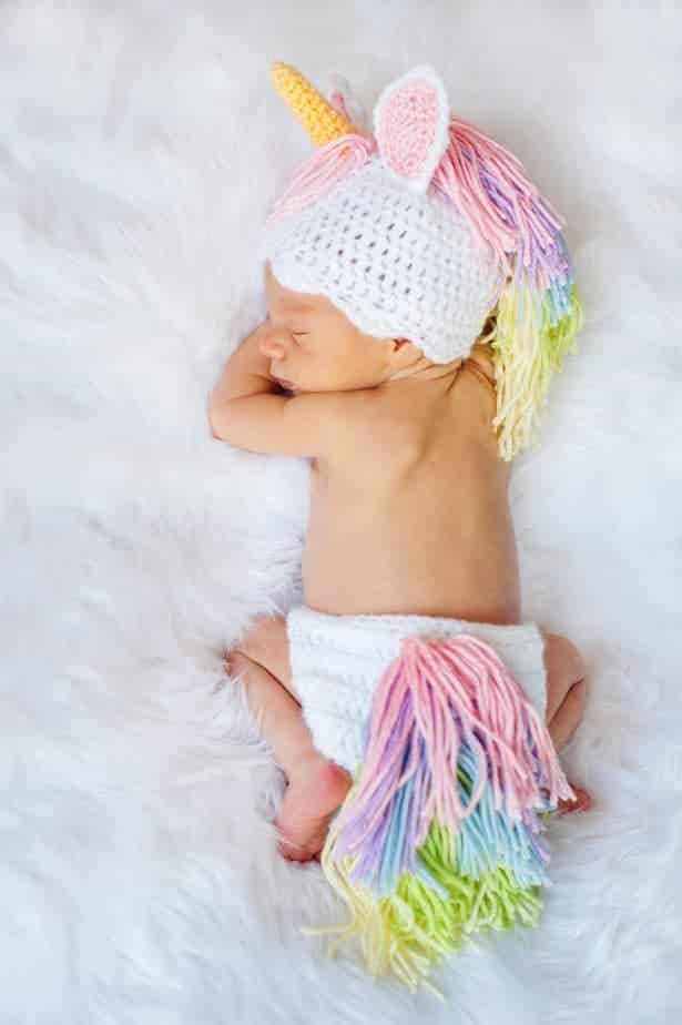 a baby is wearing a unicorn hat and diaper while laying on a white blanket