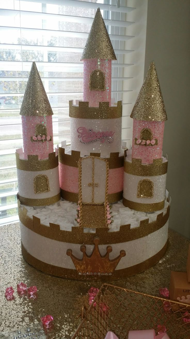 a pink and gold princess castle cake sitting on top of a table next to a window