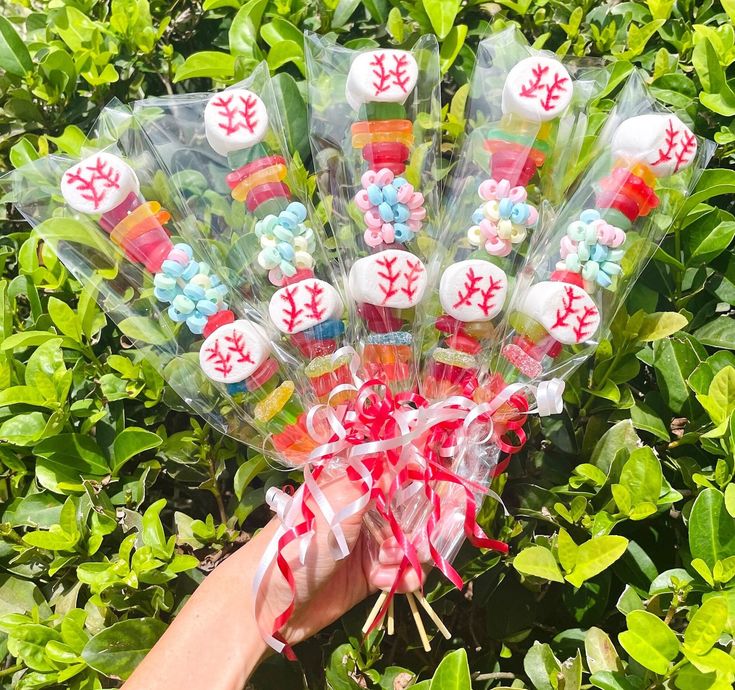 a hand holding up a bunch of candy covered in baseballs on top of green leaves