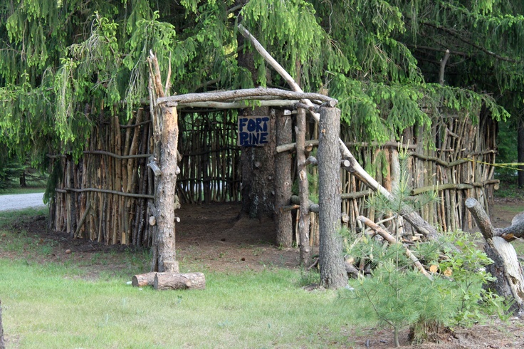 a wooden structure made out of sticks and logs in the grass with trees around it