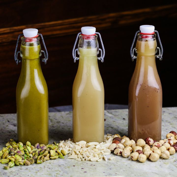 three glass bottles filled with different types of drinks next to nuts and other food items