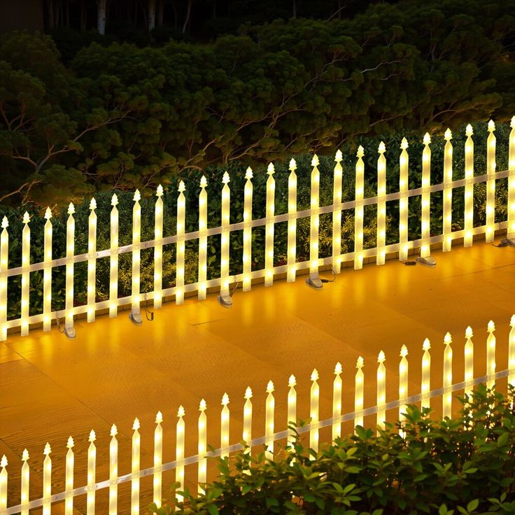 a white picket fence lit up at night with the lights on it's sides