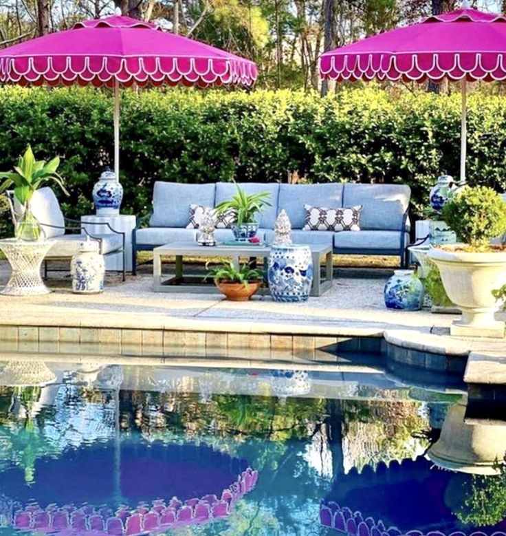 an outdoor pool with blue and white furniture under pink umbrellas next to the water