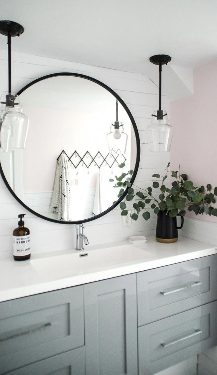 a bathroom vanity with a round mirror and plants on the counter top in front of it