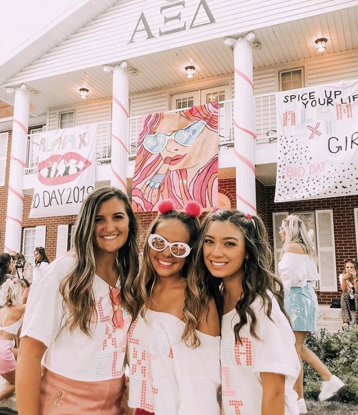 three girls standing in front of a building with pink and white decorations on the side