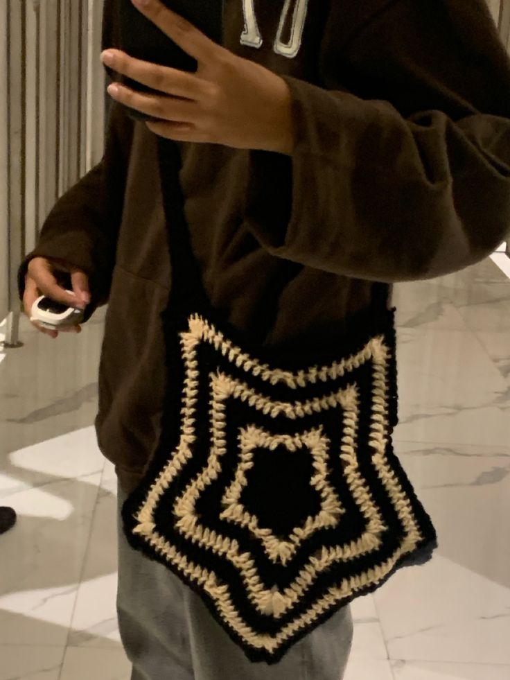 a man holding a cell phone in his hand and crocheted bag on his shoulder