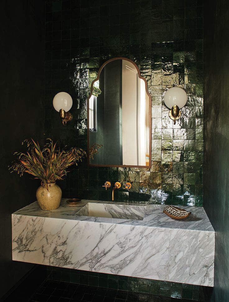 a bathroom with marble counter top and green tile on the wall, along with a vase filled with flowers