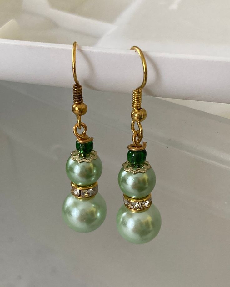 These earrings are made with light green glass pearl beads, green seed beads, rhinestone spacer beads, and metal bead caps. Handmade Bracelets Tutorial, Earring Inspo, Bridesmaid Earrings Gold, Beaded Earrings Diy, Diy Jewelry Unique, Blue Dangle Earrings, Metal Bead, Bridal Earrings Pearl, Wire Work Jewelry