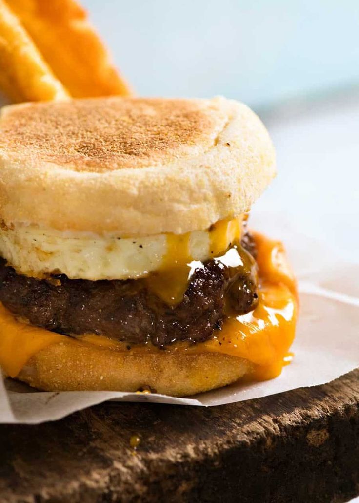 a cheeseburger with an egg and meat patty on it, sitting on a piece of wax paper