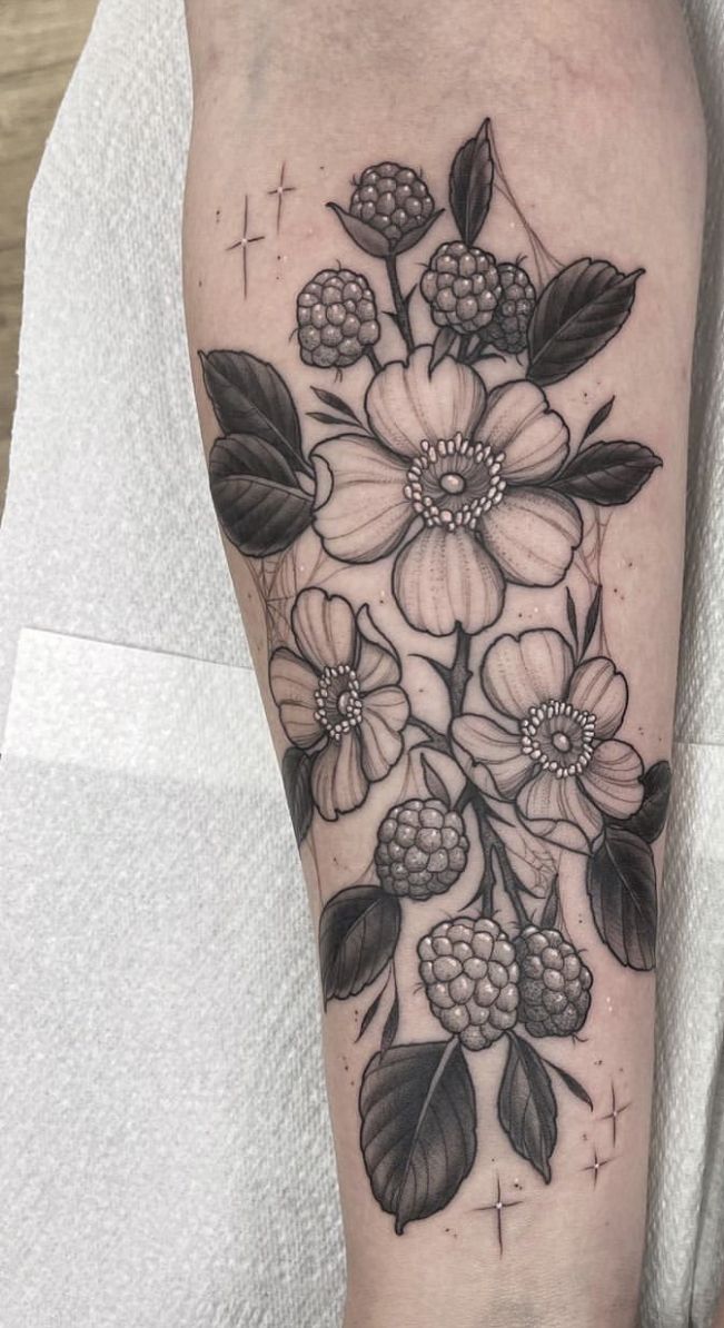 a black and white flower tattoo on the left arm, with leaves and berries around it