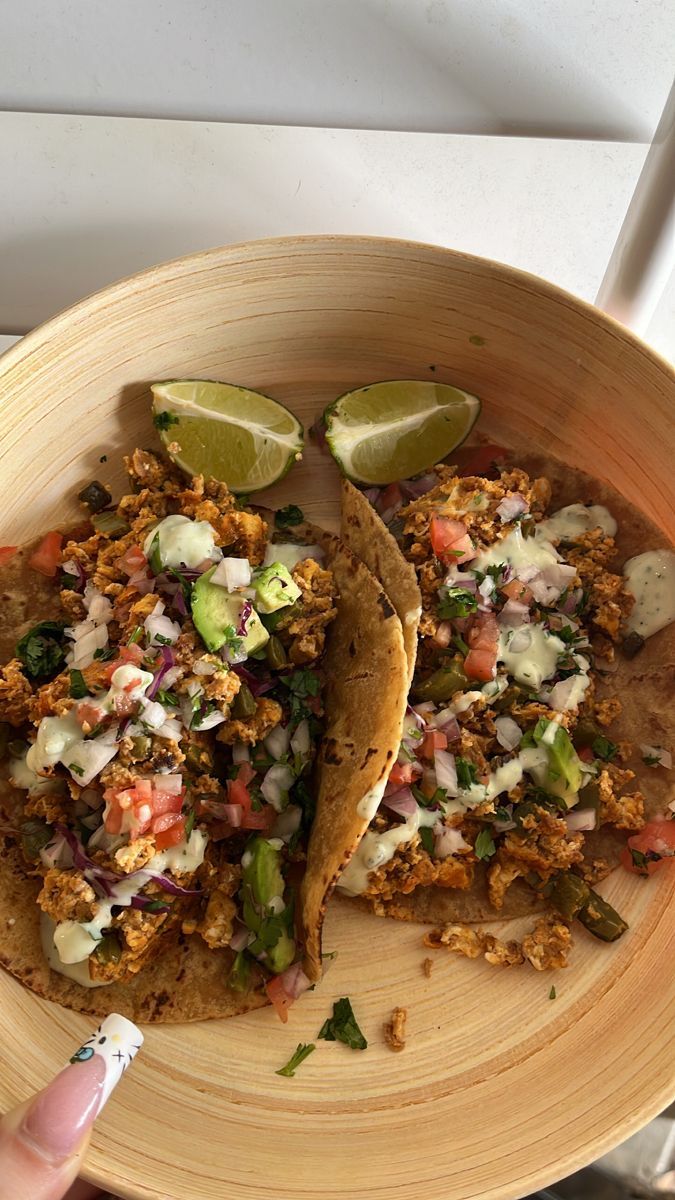 two tacos in a wooden bowl with lime wedges on the side and salsa