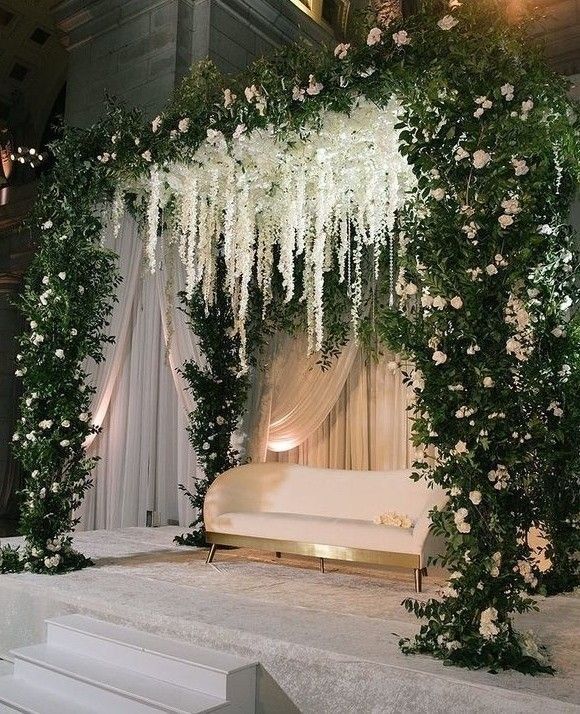 an outdoor ceremony with white flowers and greenery hanging from the ceiling, along with a couch