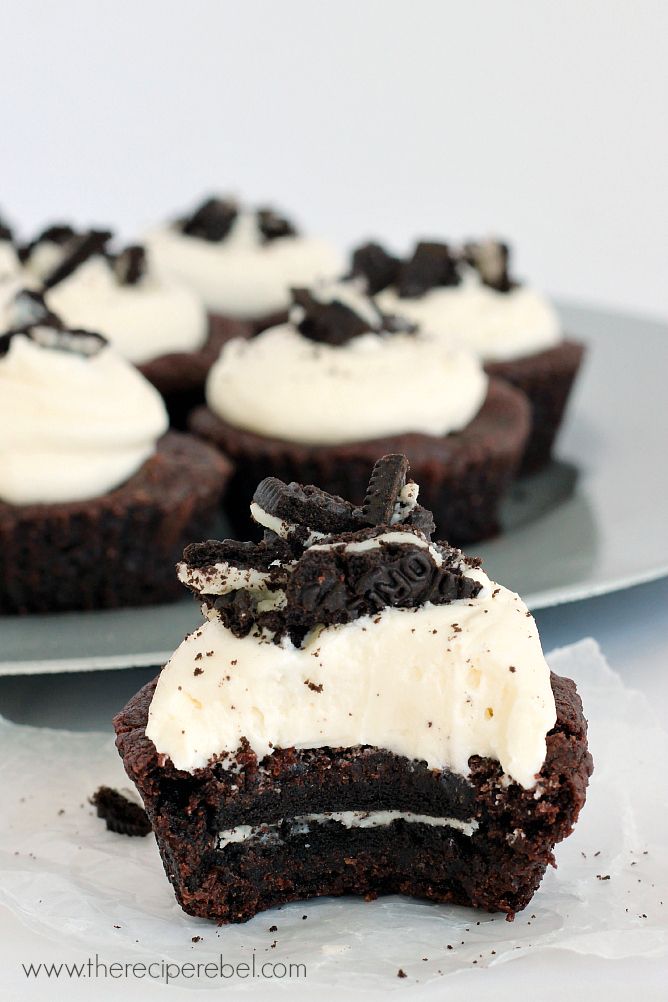 two chocolate cupcakes with white frosting and oreo cookies on top, one half eaten