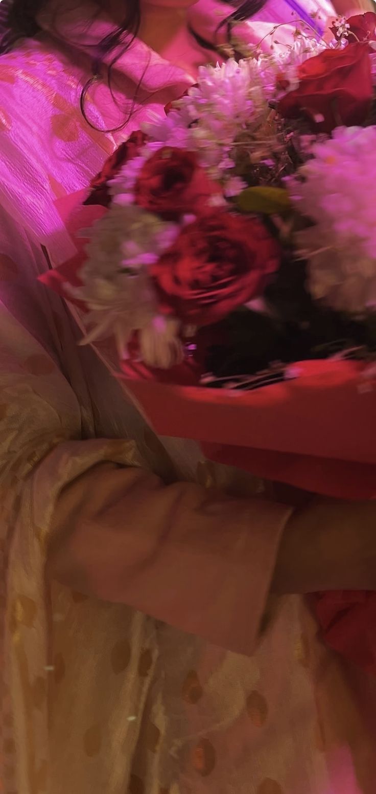 a woman holding a bouquet of red and white flowers in her hands with pink lighting behind her