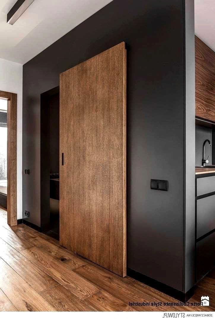 an empty room with wood flooring and black walls, two doors open to the kitchen