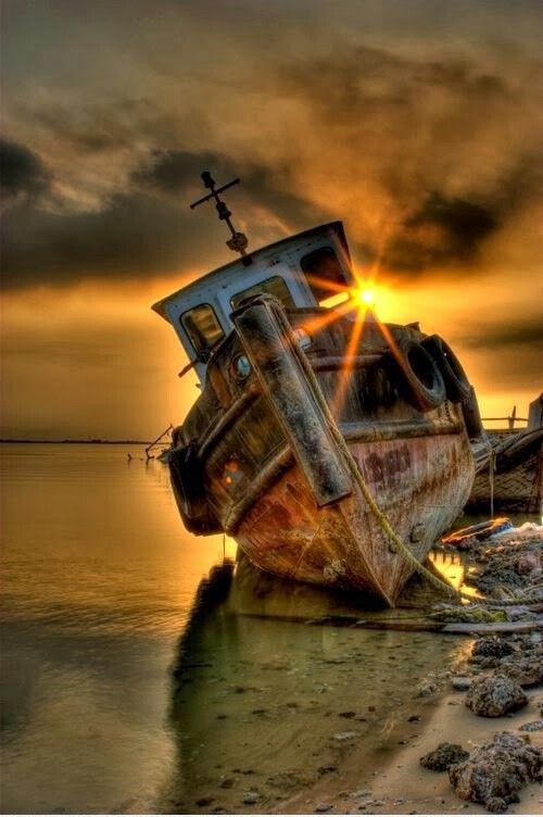 an old boat sitting on top of a beach next to the ocean under a cloudy sky