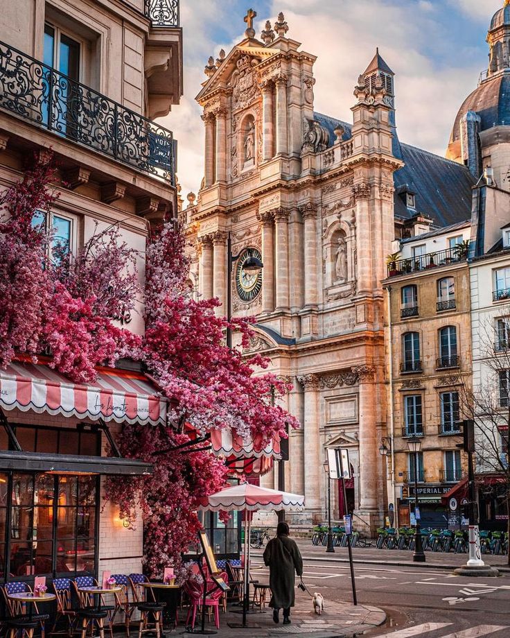 a woman is walking down the street in front of some buildings with pink flowers on them