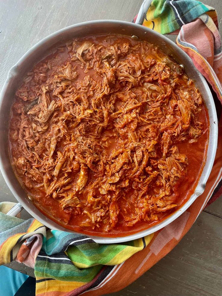 a large pot filled with meat and sauce on top of a wooden table next to napkins