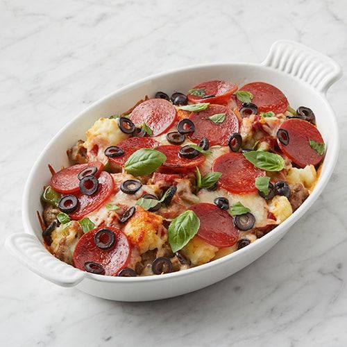 a white casserole dish with pepperoni, olives, and other toppings