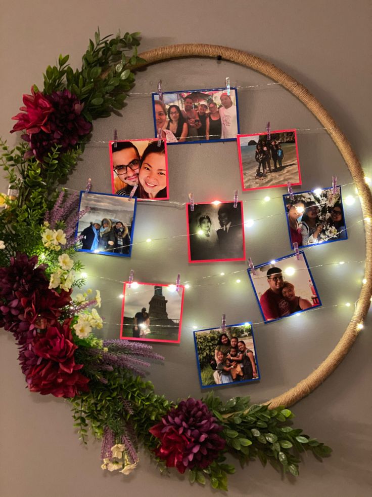 a circular wall hanging with pictures and lights on it, surrounded by flowers and greenery