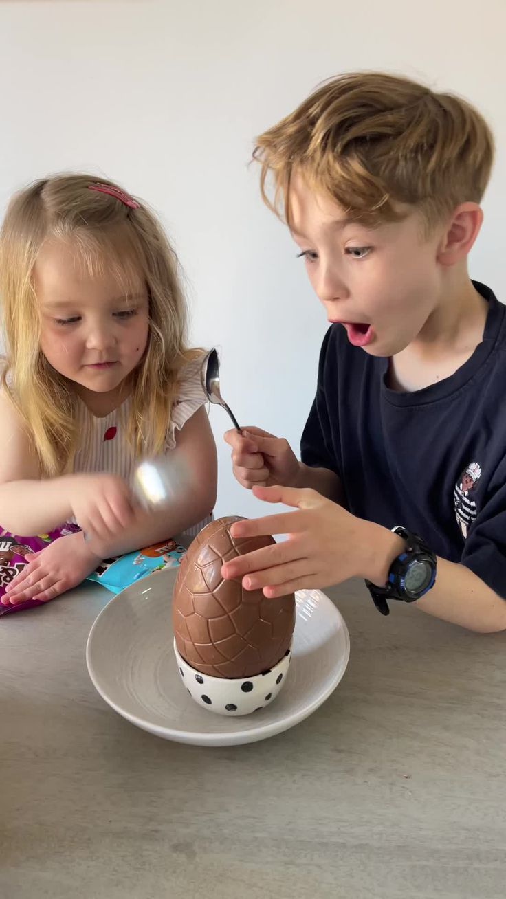 two children sitting at a table with an easter egg