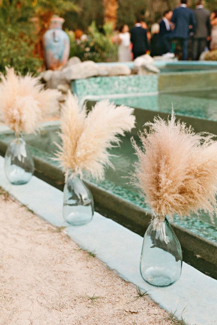 three vases with flowers in them sitting on the ground next to a fountain at a wedding