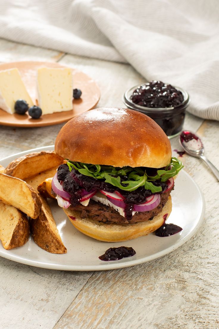 a hamburger and fries on a plate with some blueberry sauce in the bowl next to it