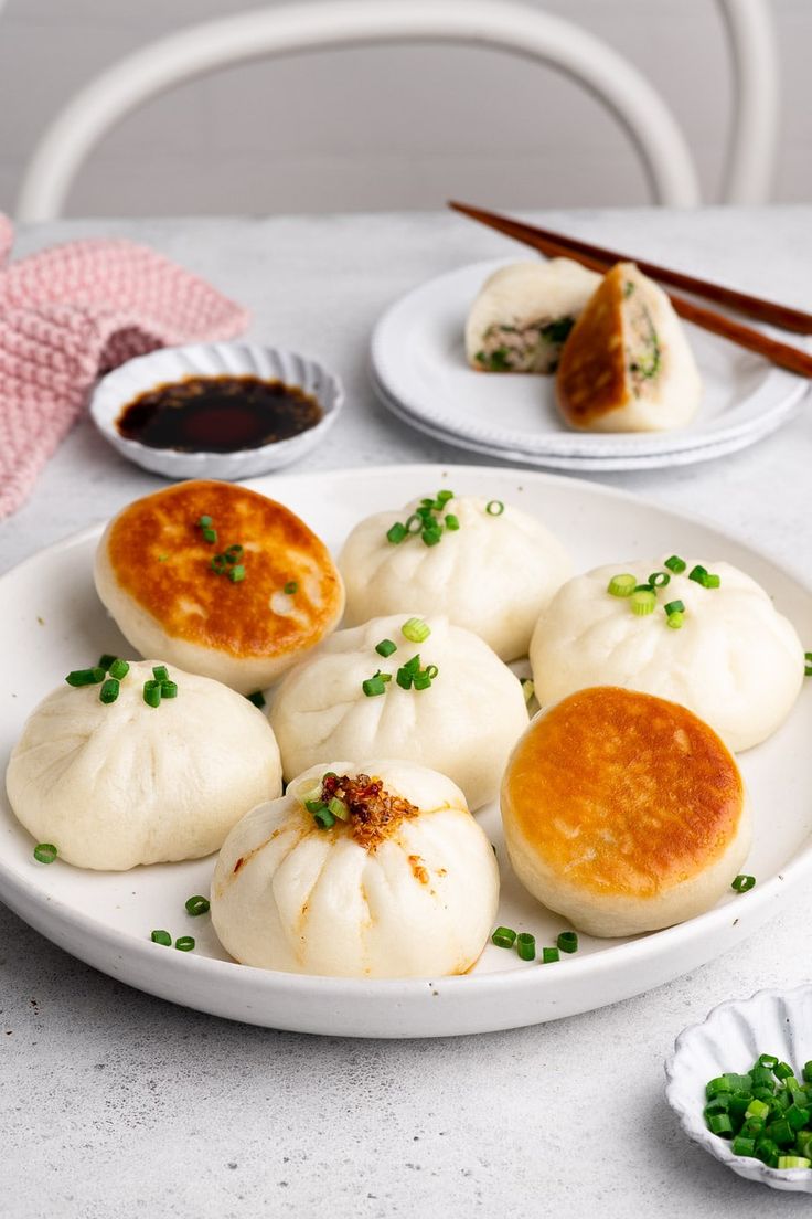 small steamed dumplings on a white plate with chopsticks and dipping sauce in the background