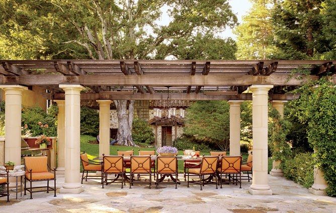 an outdoor dining area with tables and chairs under a pergolated arbor, surrounded by greenery