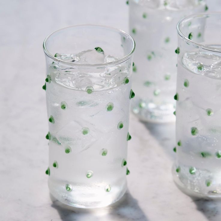 three glasses filled with water and ice on top of a white countertop next to each other