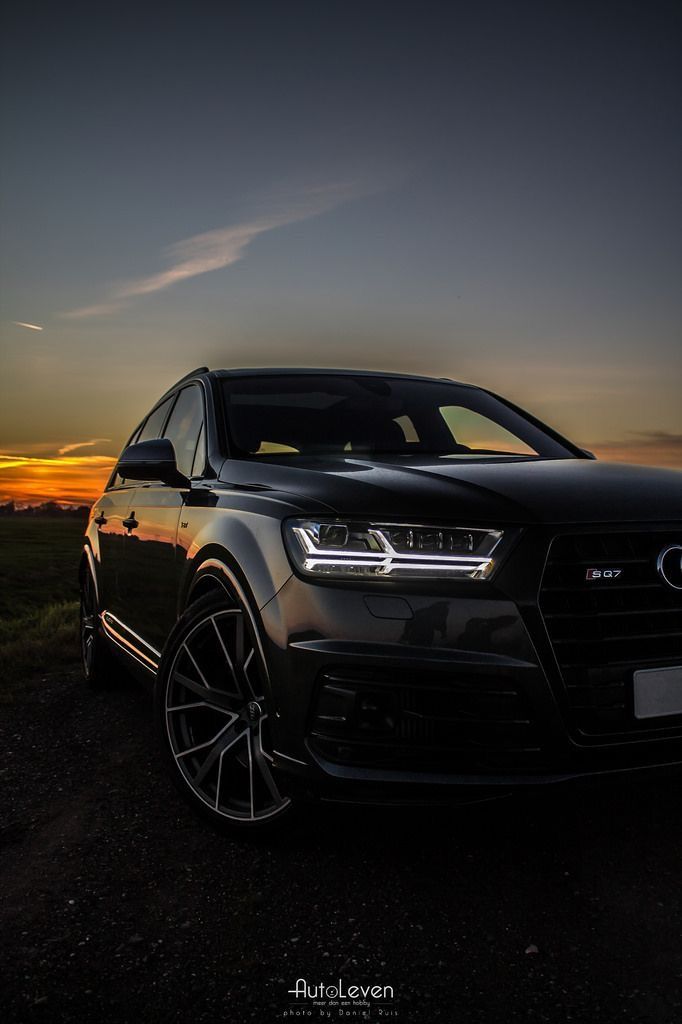 the front end of a black car parked on a dirt road at sunset with an orange sky in the background