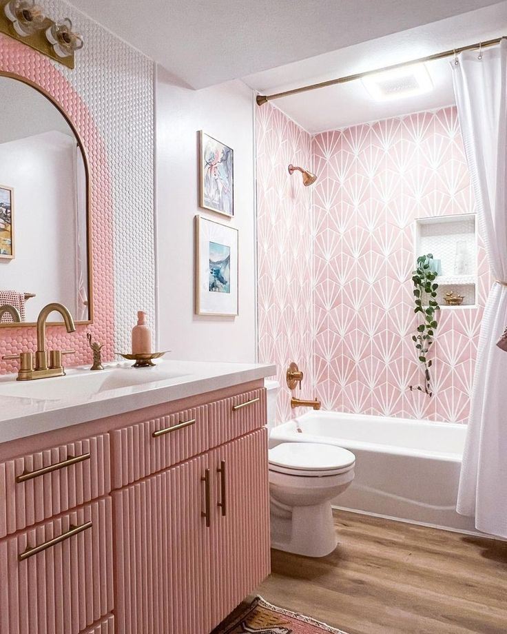 a bathroom decorated in pink and white with gold accessories on the vanity, shower curtain, toilet seat cover, rug and mirror