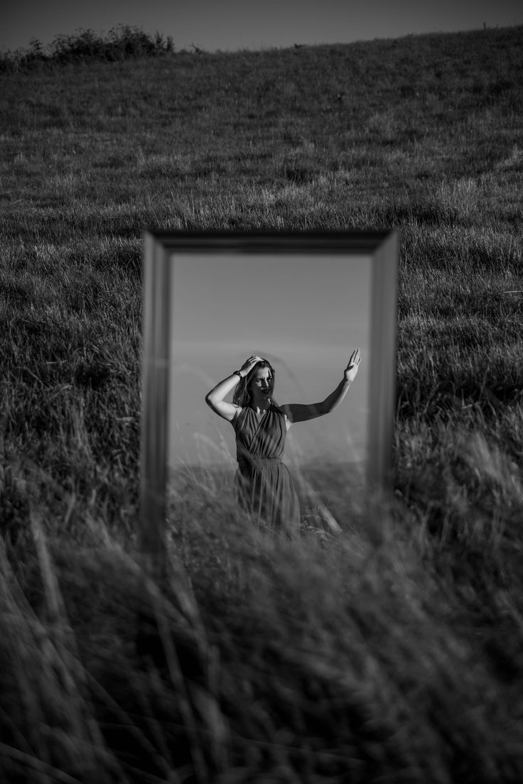 a black and white photo of a woman standing in tall grass with her hand on her head