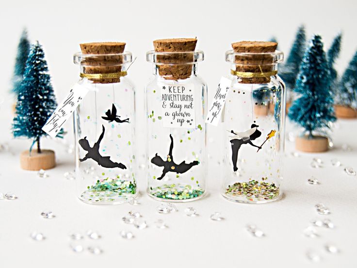 four glass bottles filled with tiny trees and some writing on the top one is labeled peter pan tinkerbell