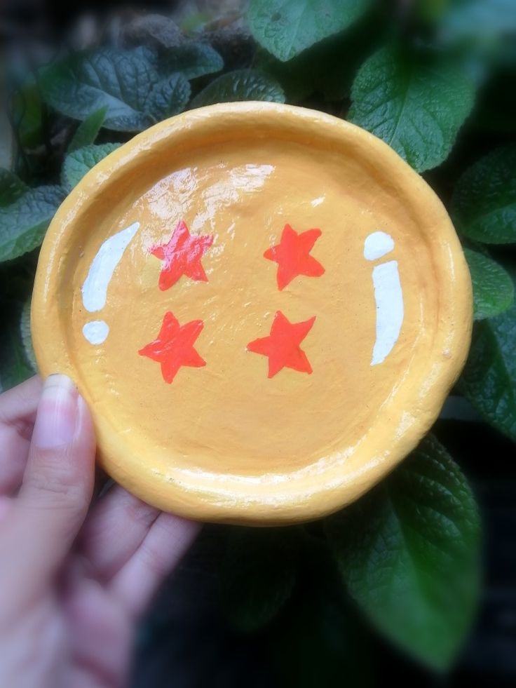 a hand holding a yellow bowl with red stars painted on the side and green leaves in the background