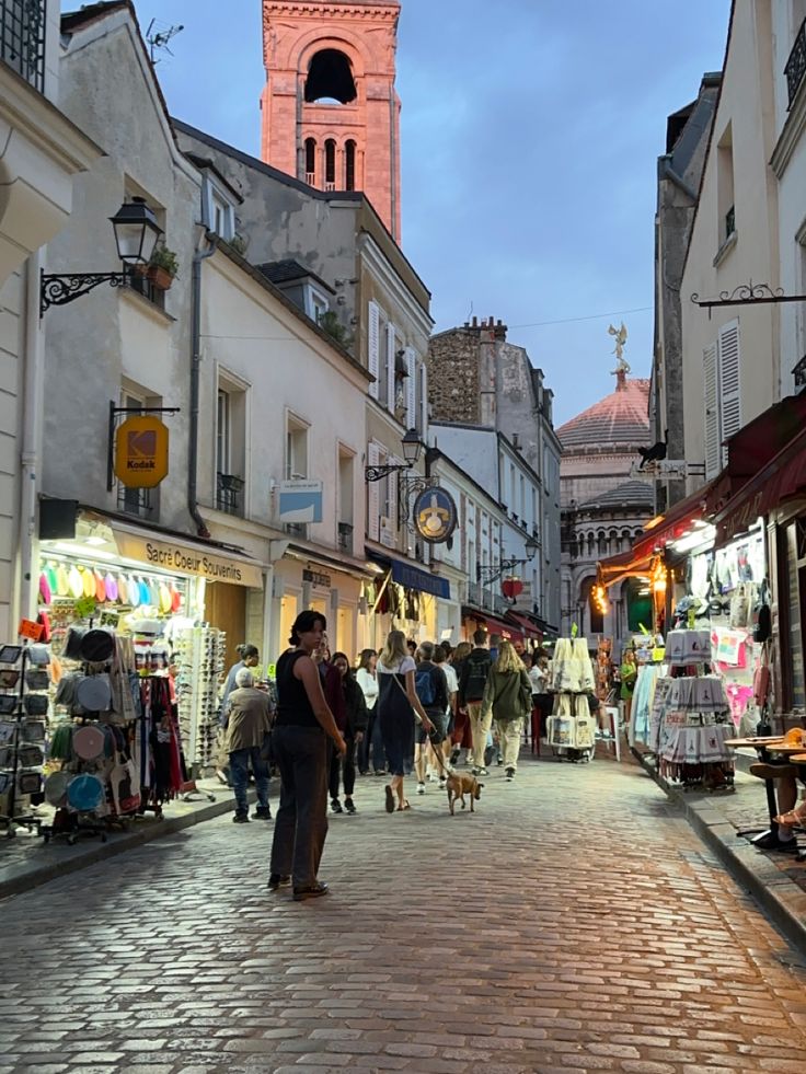 people are walking down the street in front of shops and buildings with a clock tower